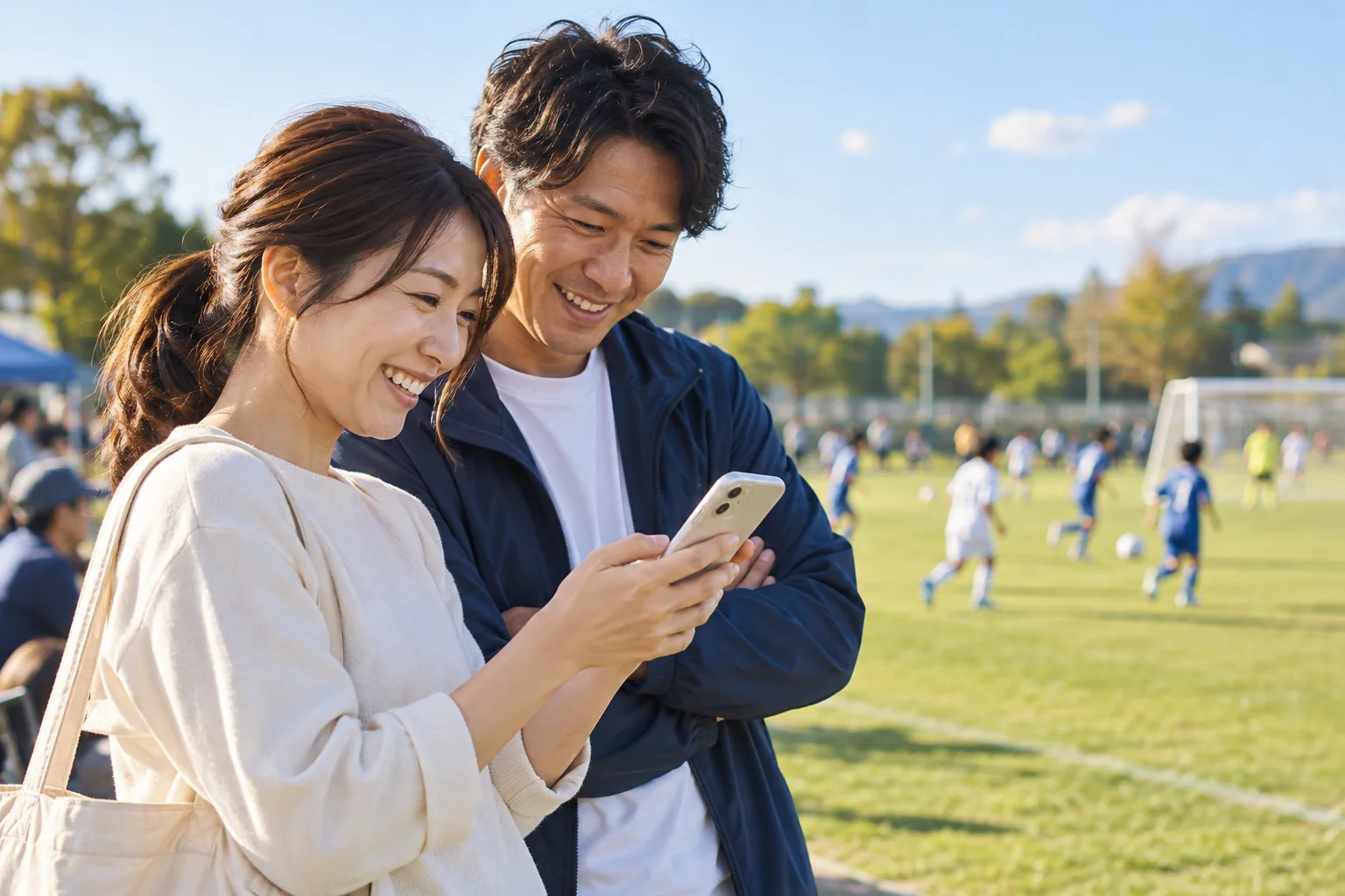 グラウンド脇でスマートフォンを確認する保護者・スタッフのイメージ